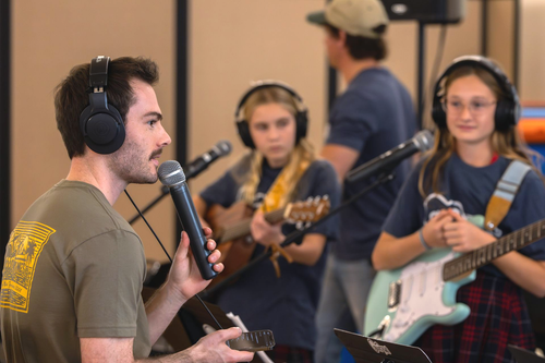 A music teacher gives instructions to kids holding instruments during band practice.