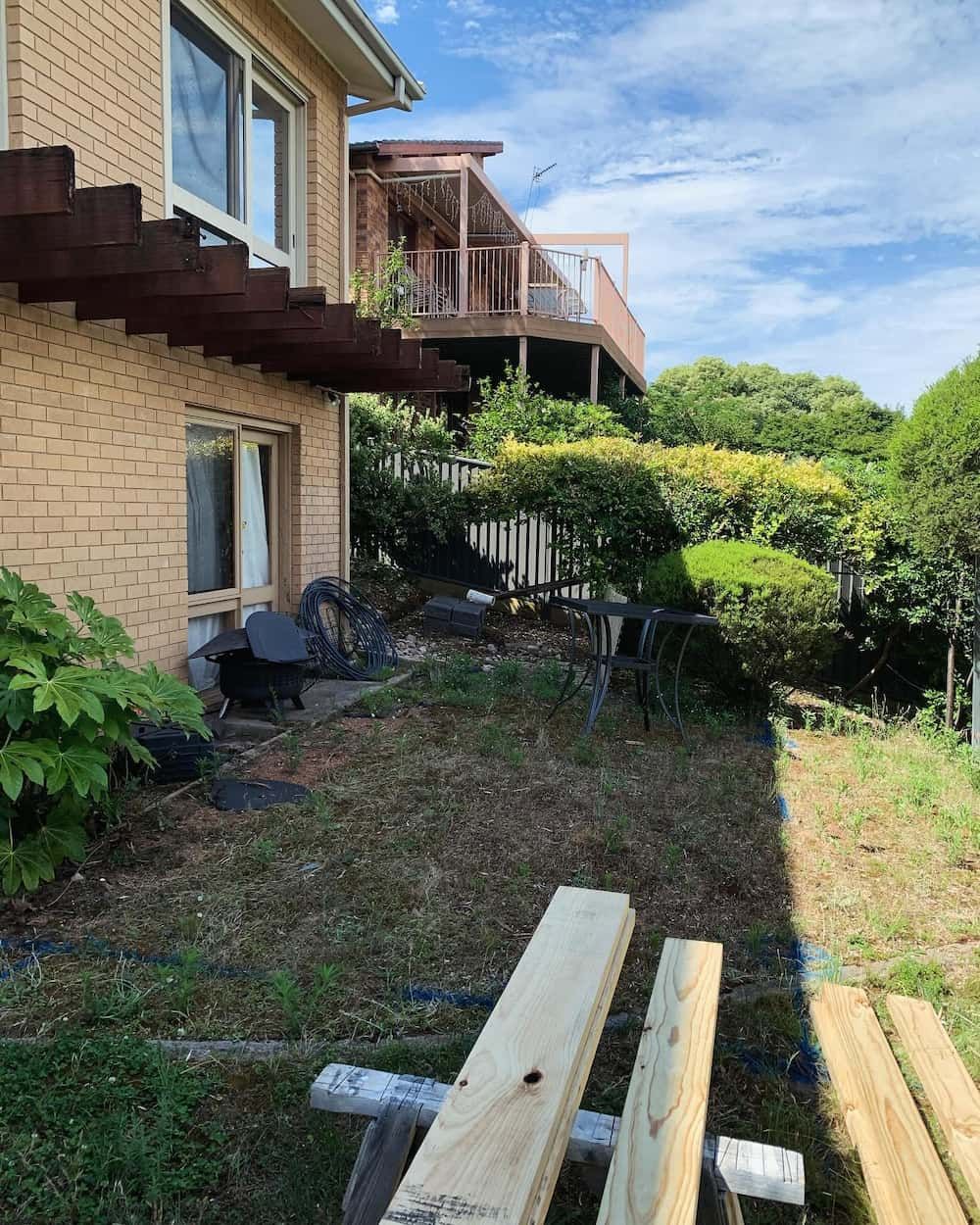 A wooden bench is sitting in front of a brick house. — Renovo Contractors In Monash, ACT