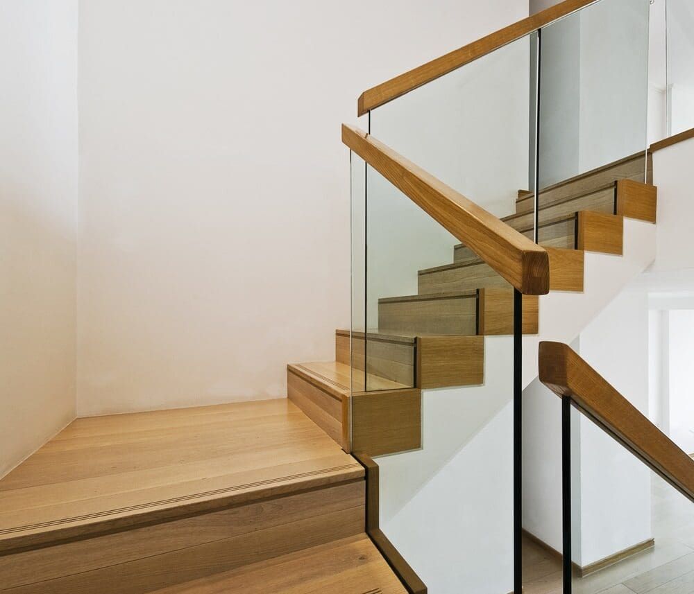 A Wooden Staircase With A Glass Railing In A House — Renovo Contractors In Monash, ACT