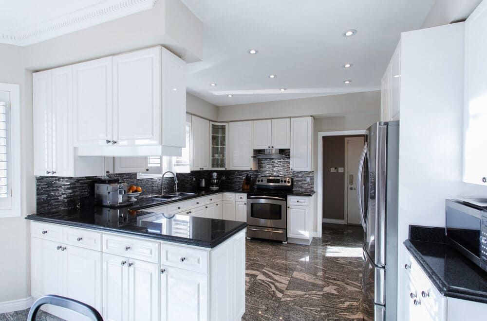 A Kitchen With White Cabinets, Black Counter Tops, And Stainless Steel Appliances — Renovo Contractors In Monash, ACT