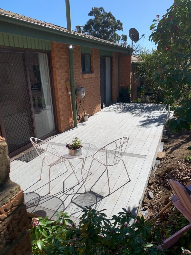 A Patio With A Table And Chairs In Front Of A Brick House — Renovo Contractors In Monash, ACT