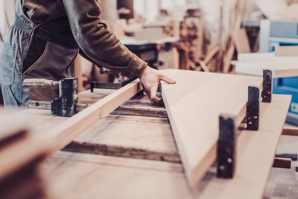 A Man Is Working On A Piece Of Wood In A Workshop — Renovo Contractors In Monash, ACT