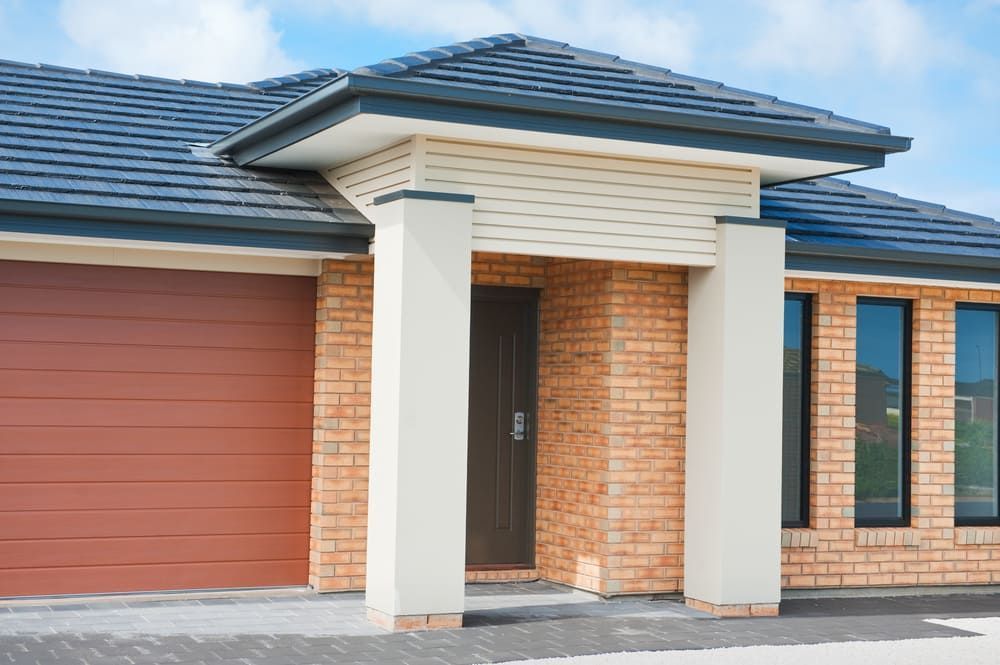A Brick House With A Red Garage Door And A Black Roof — Renovo Contractors In Monash, ACT