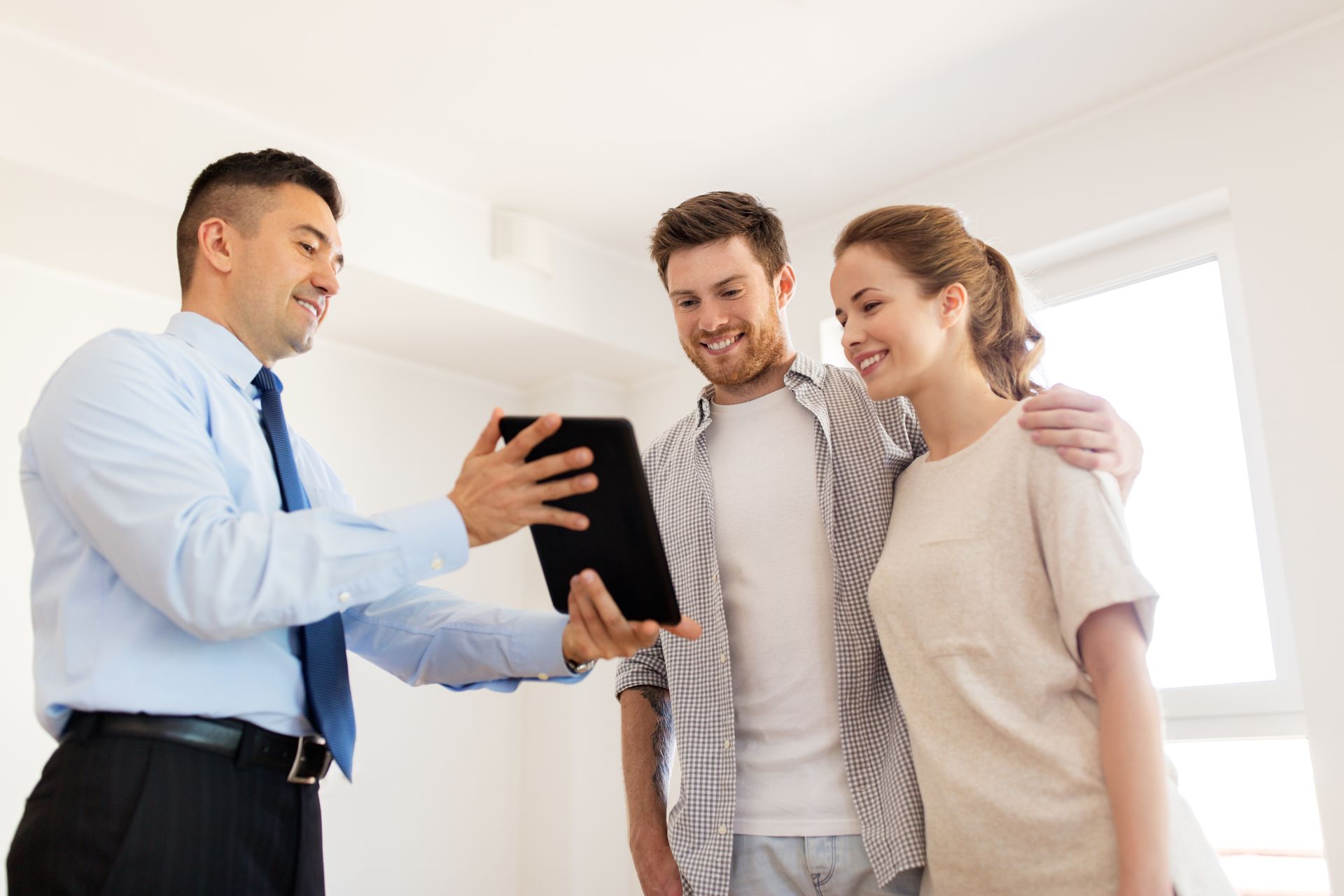 Real estate agent showing a couple a tablet, possibly displaying property details in a bright room.