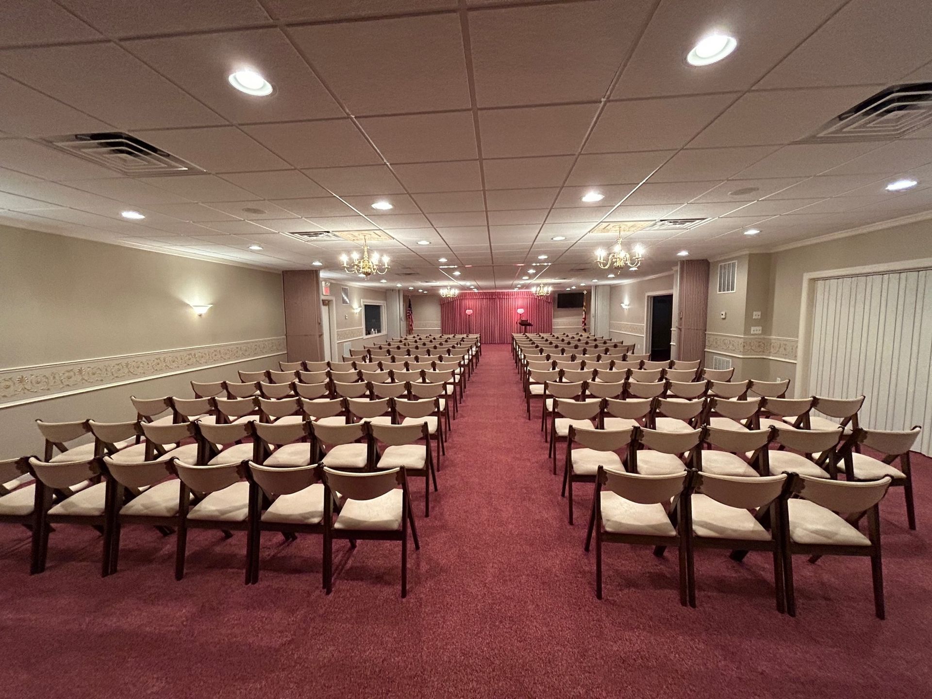 Rows of chairs in an event room, red carpet, cream walls, and overhead lighting.