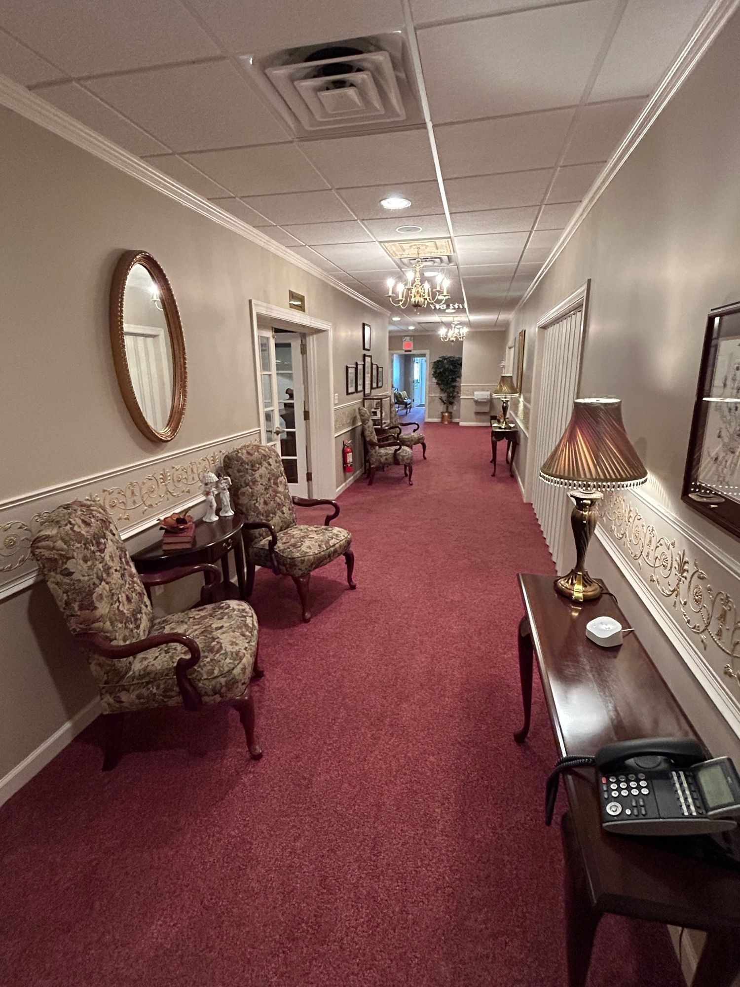 Long hallway with red carpet, chairs, and lamps.