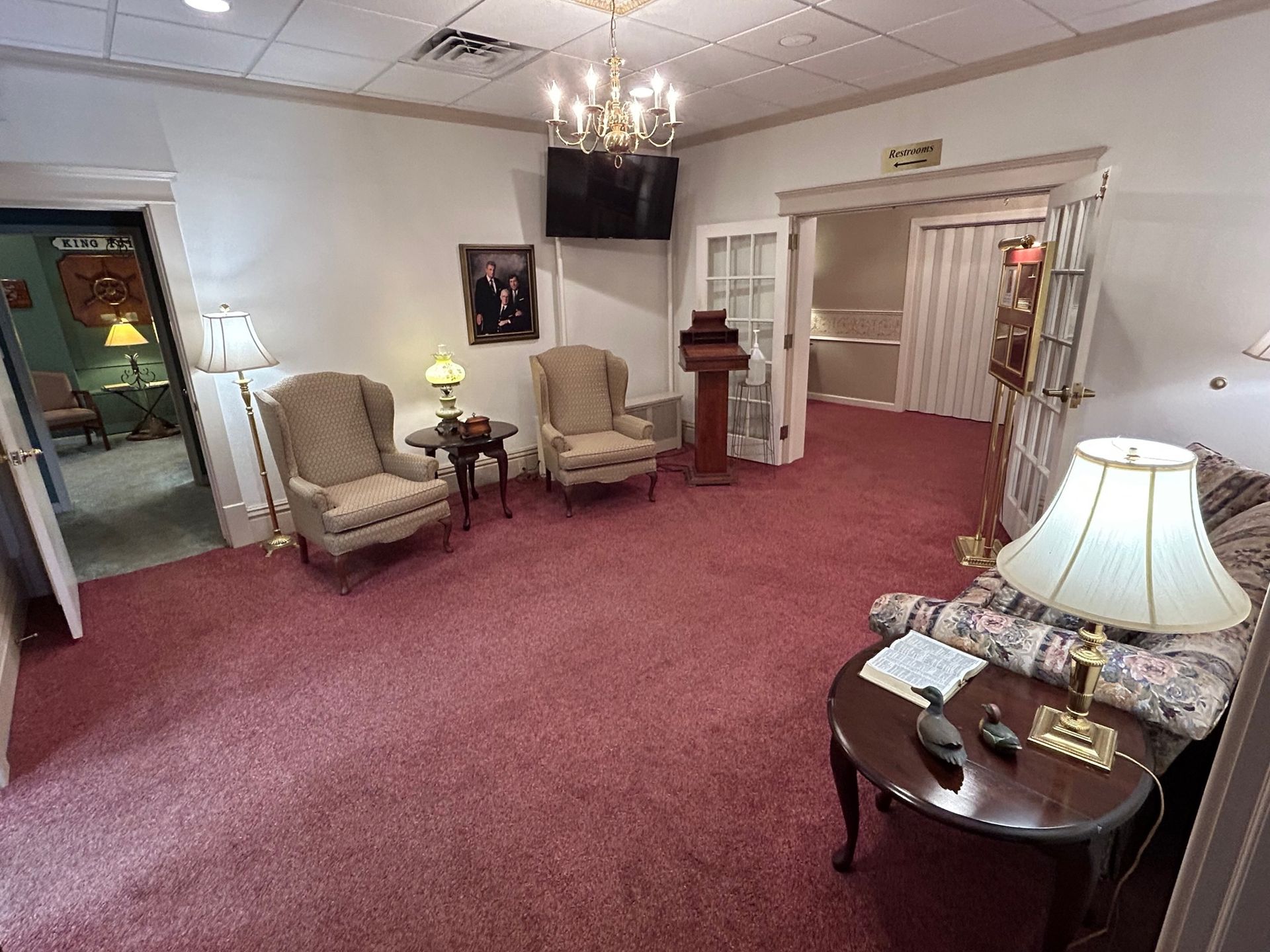 Funeral home waiting area with chairs, lamps, and a red carpet.