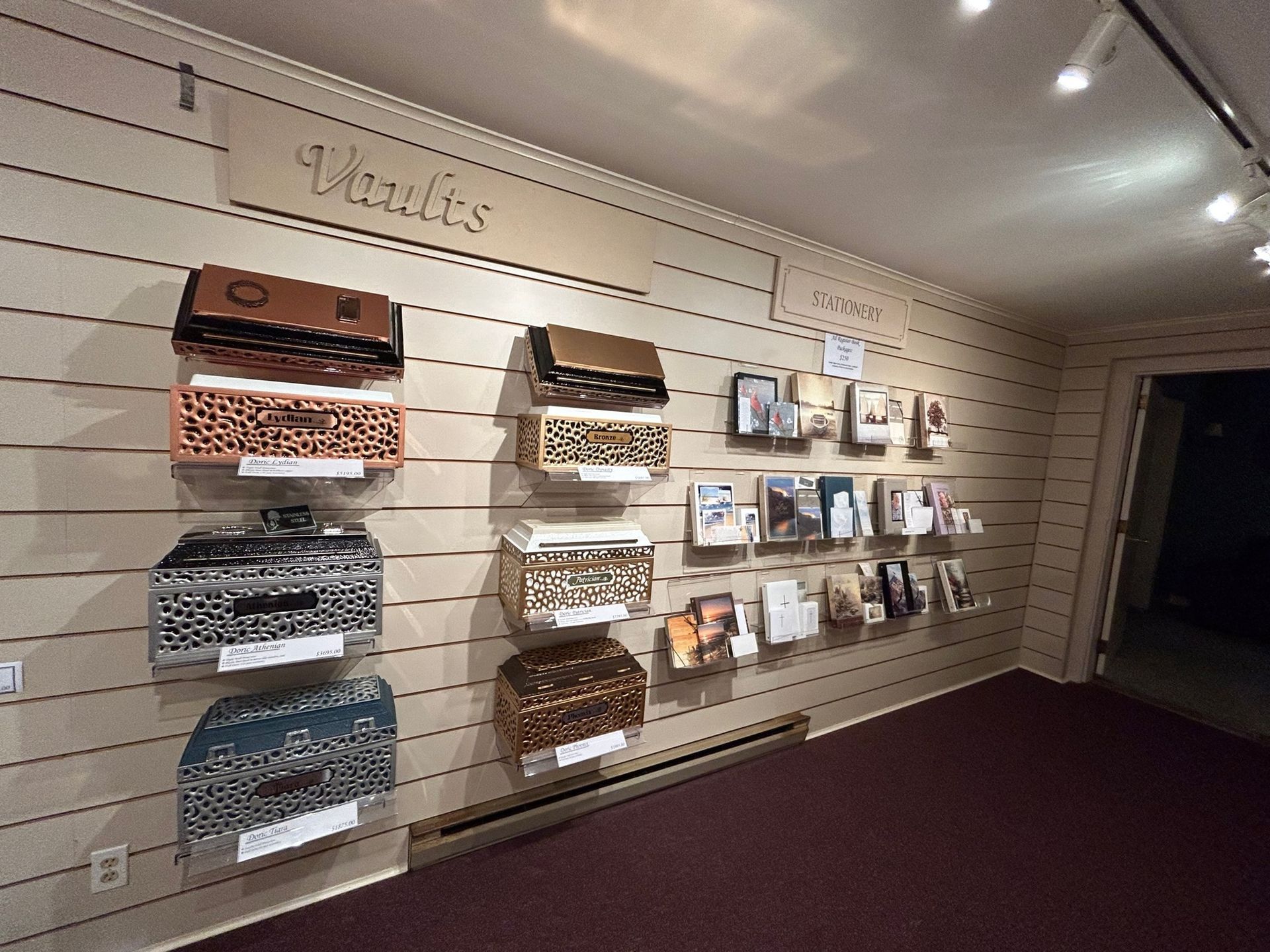 Display of burial vaults in a shop. Vaults are in various colors and designs, mounted on a wall.