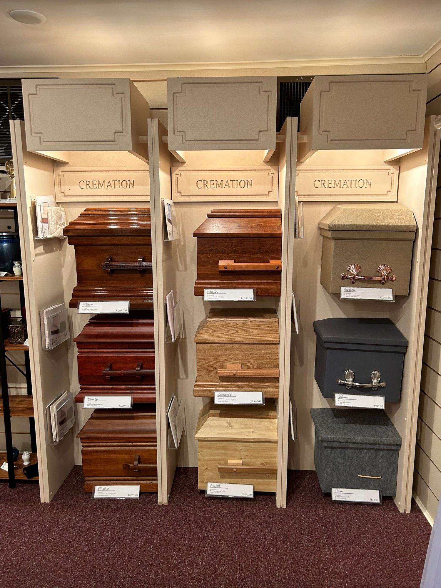 Caskets displayed in a showroom, arranged on shelves. Different colors and styles are shown.