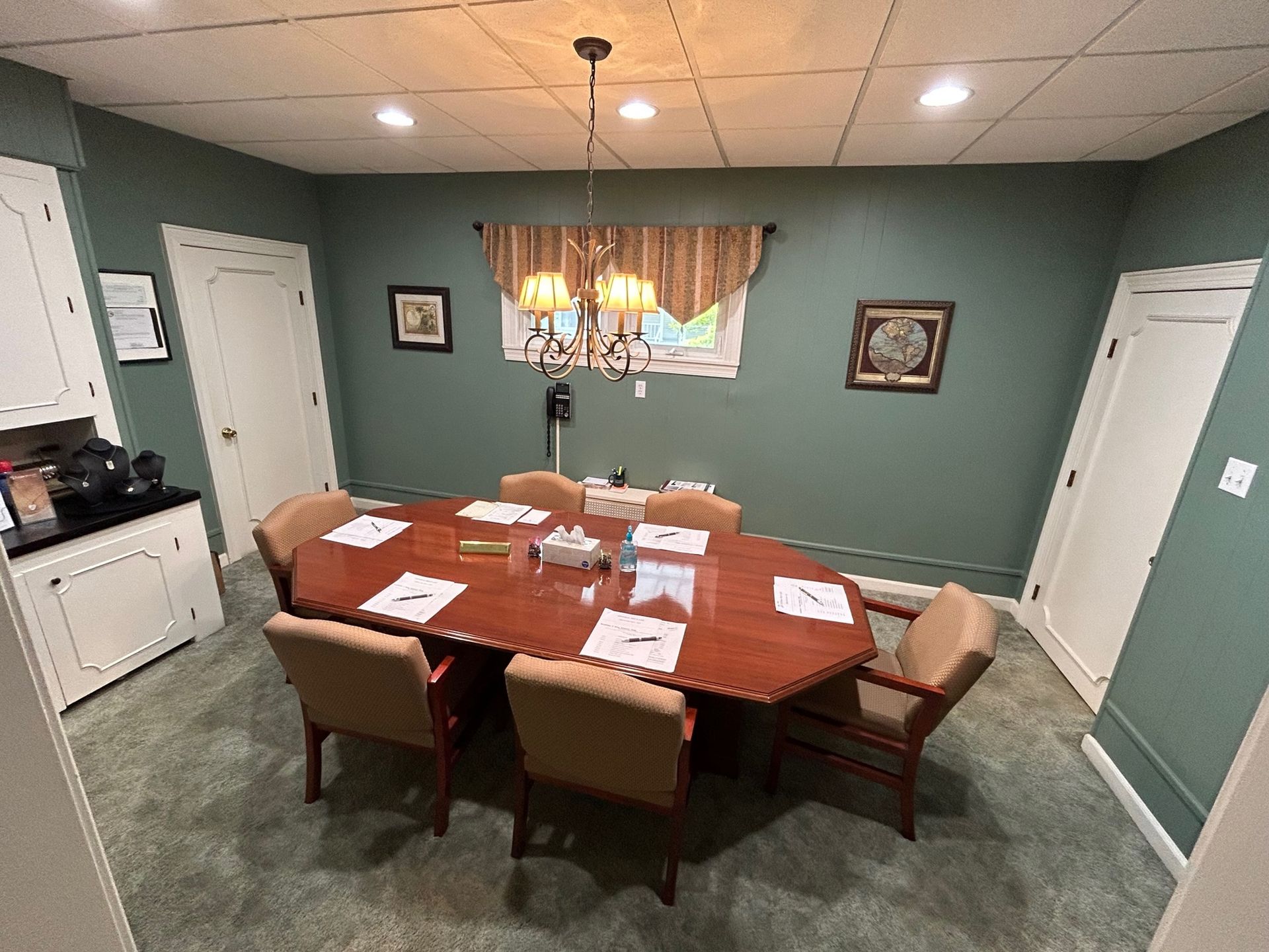 Conference room with octagon table, beige chairs, green walls, white cabinets, and a chandelier.