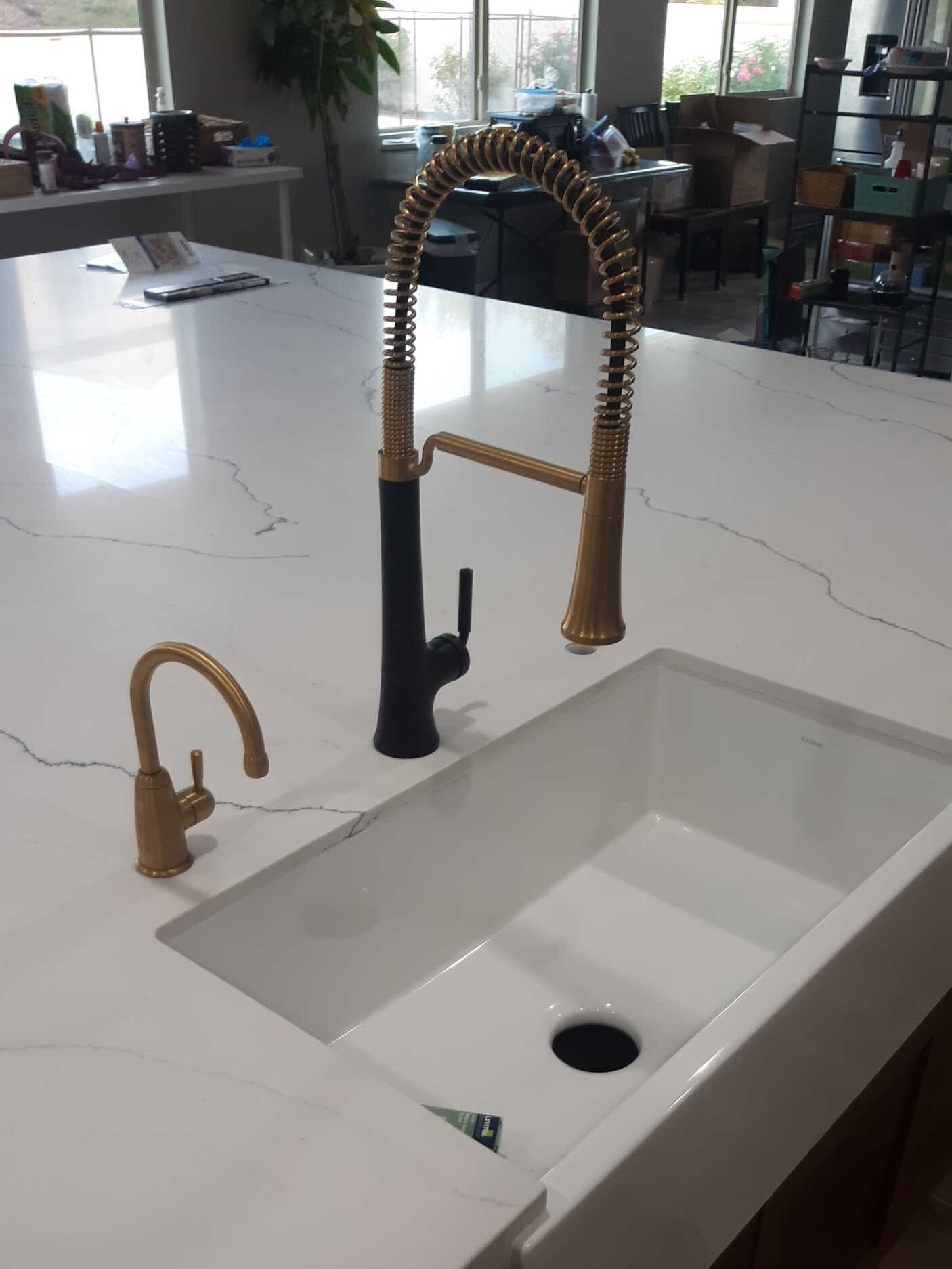 A kitchen sink with a black faucet and a gold faucet.