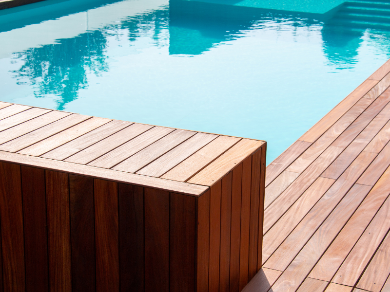 A wooden deck with a swimming pool in the background