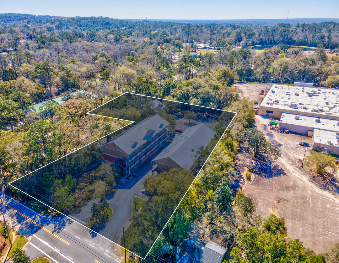An aerial view of a large building surrounded by trees and a road.