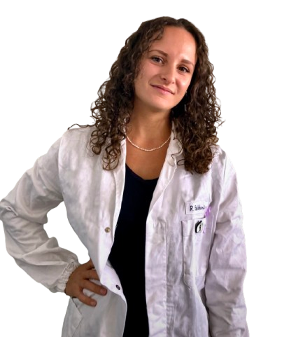 Donna con capelli castani ricci che indossa un camice da laboratorio, sorride e posa.