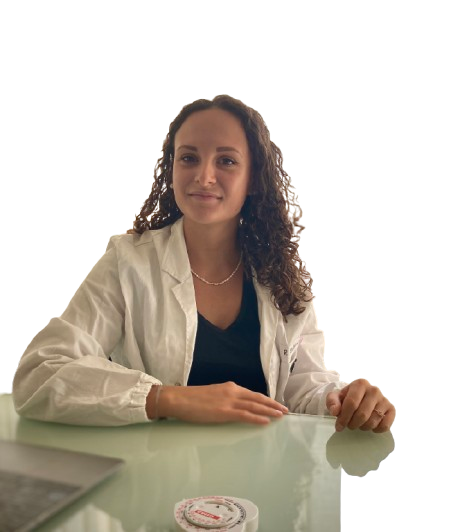 Una donna in camice bianco è seduta alla scrivania e guarda avanti.