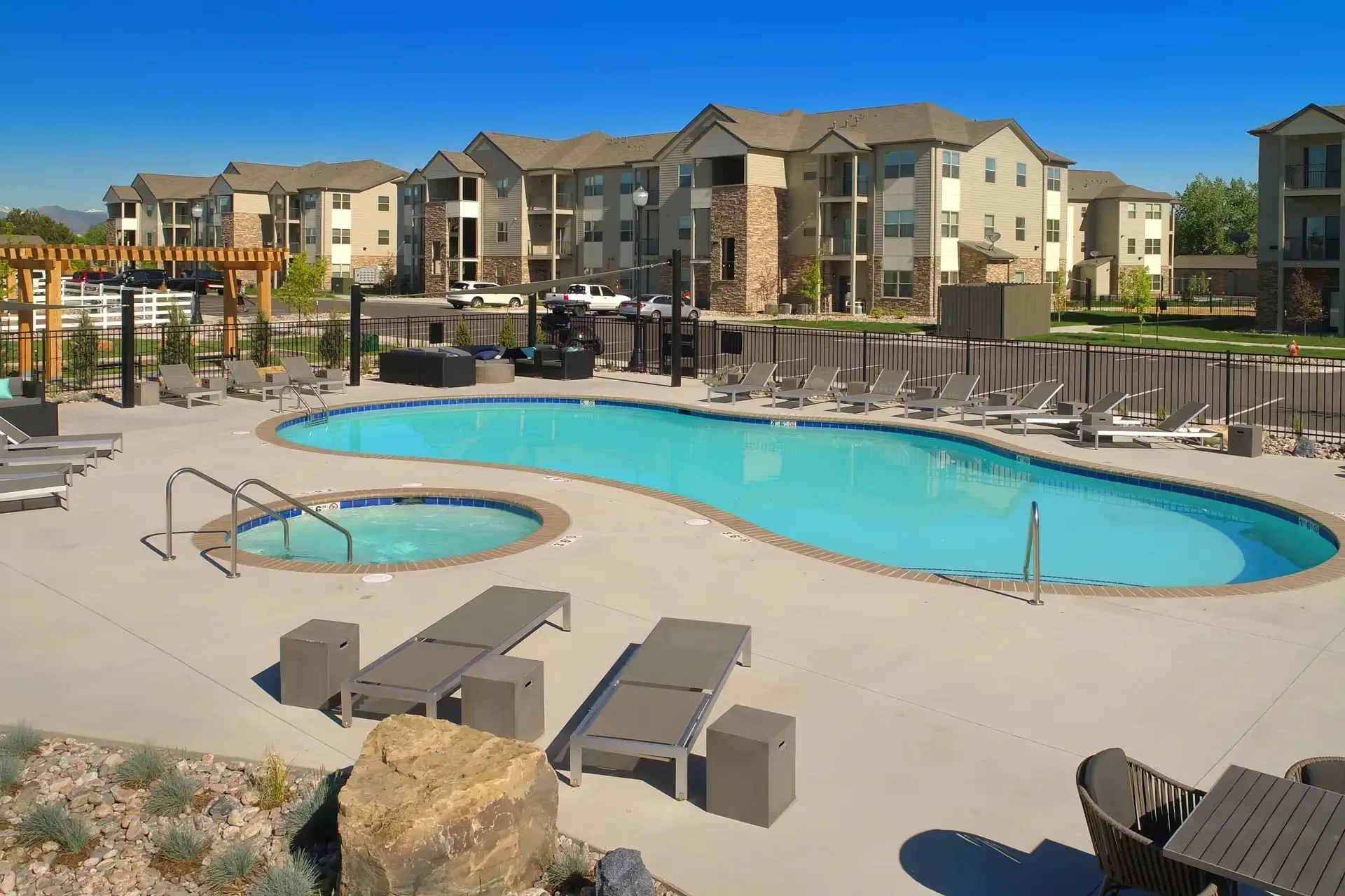 Luxury apartment complex with an inviting swimming pool and hot tub, surrounded by lounge chairs and outdoor seating.
