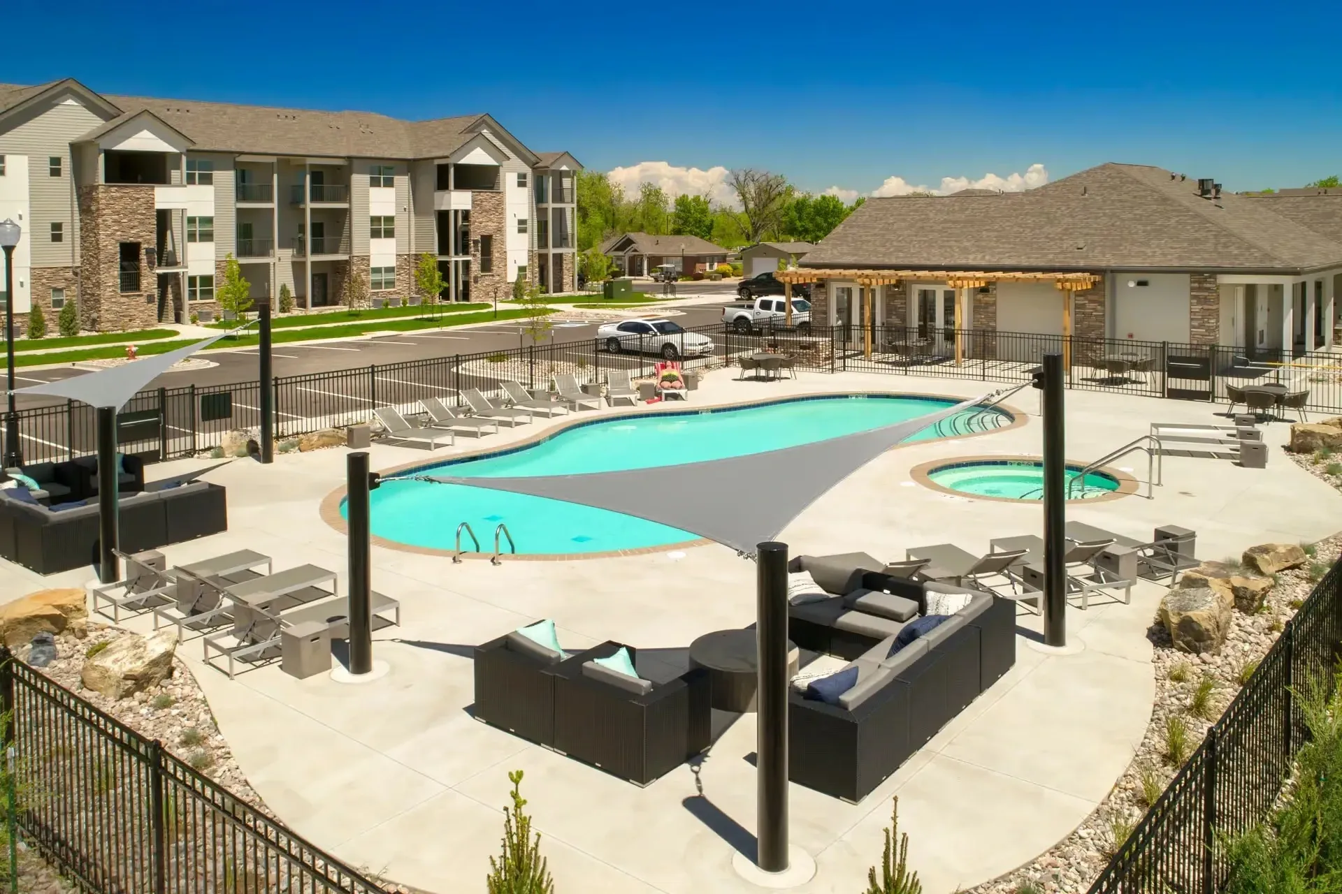 Apartment complex with a large outdoor swimming pool and hot tub, surrounded by lounge chairs and seating areas.