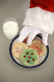 santa claus is reaching for a plate of cookies and a glass of milk .