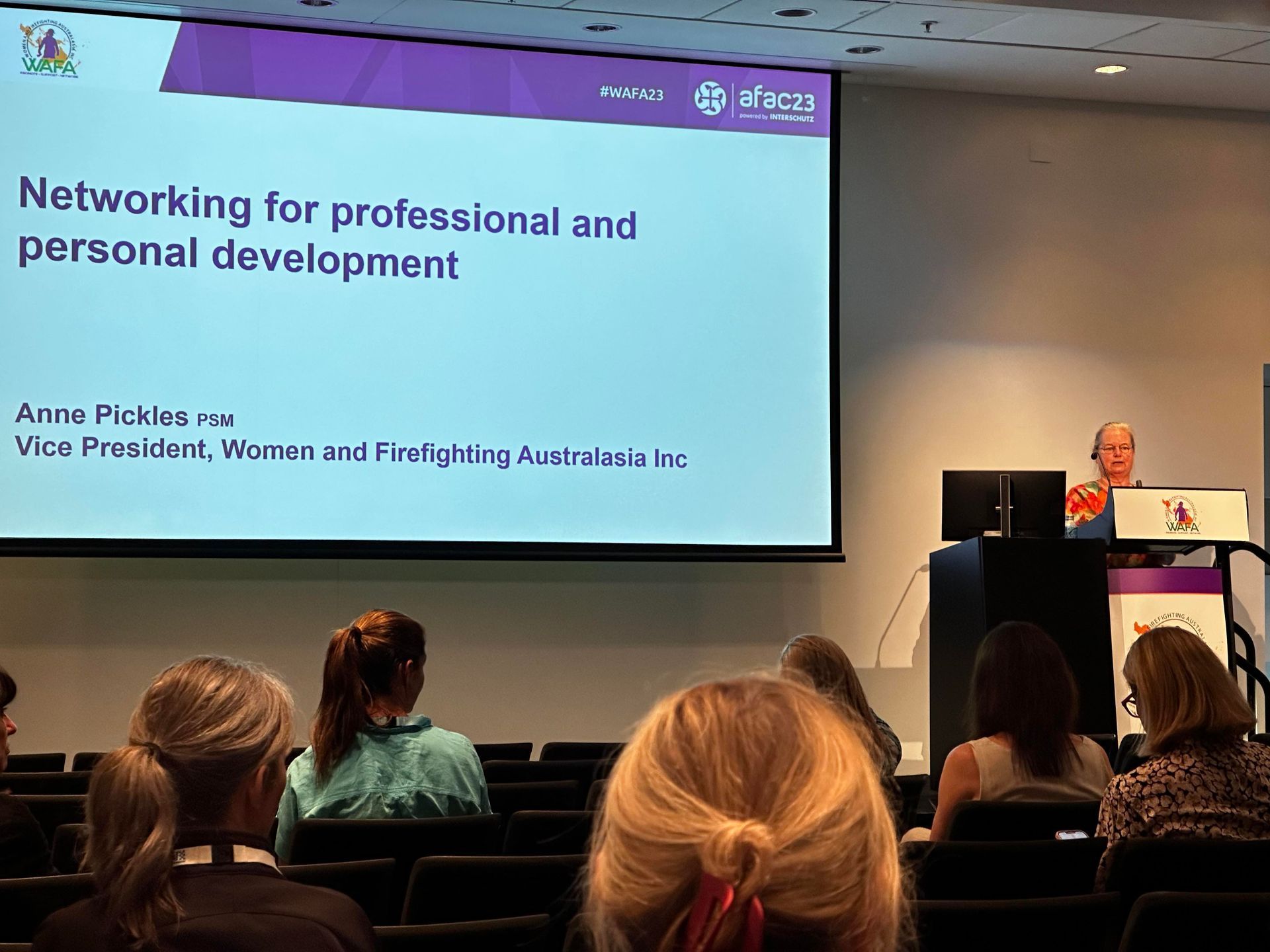 A woman speaking at a conference, giving a presentation on networking. Audience members sit in front.