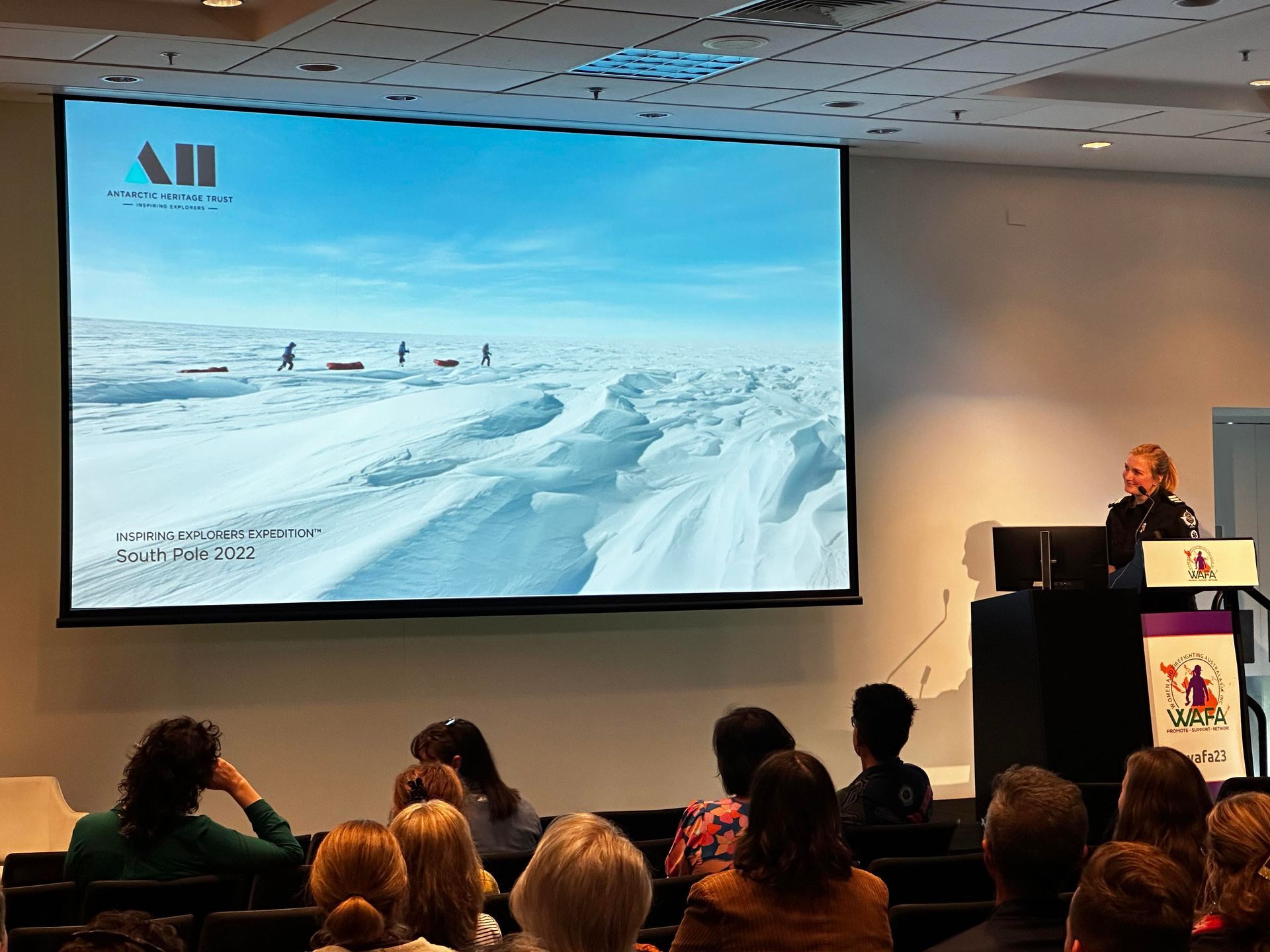 A person giving a presentation with a snowy landscape on the screen, audience members watching.