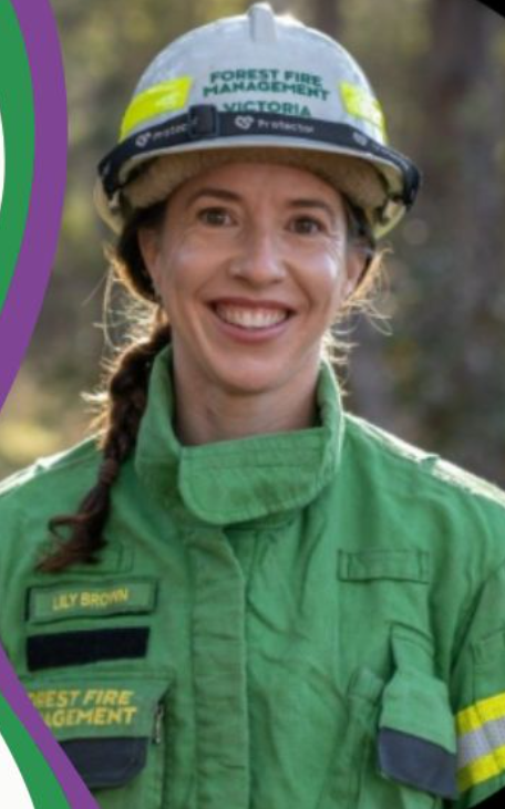 Female firefighter in green uniform and helmet, smiling.