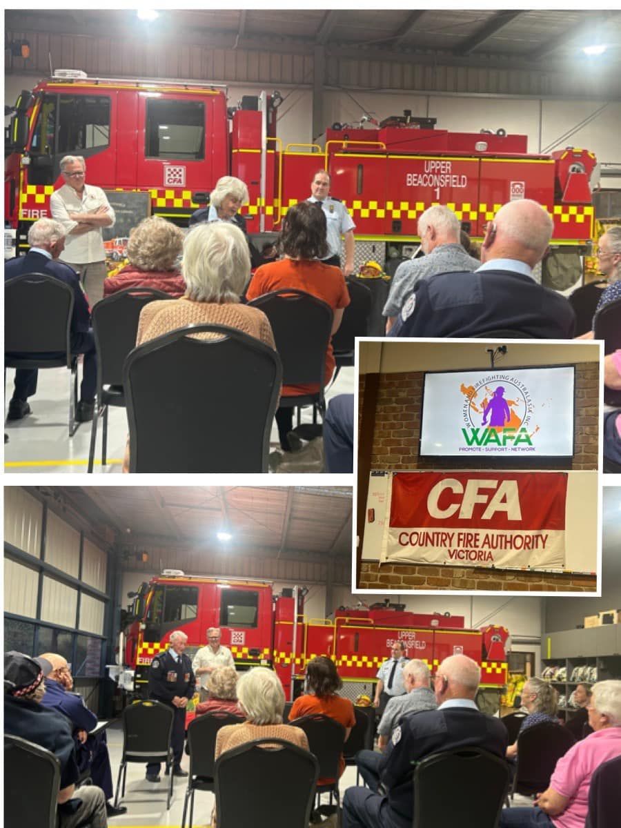Meeting at fire station. People listening to speakers in front of fire trucks, CFA and community flags visible.