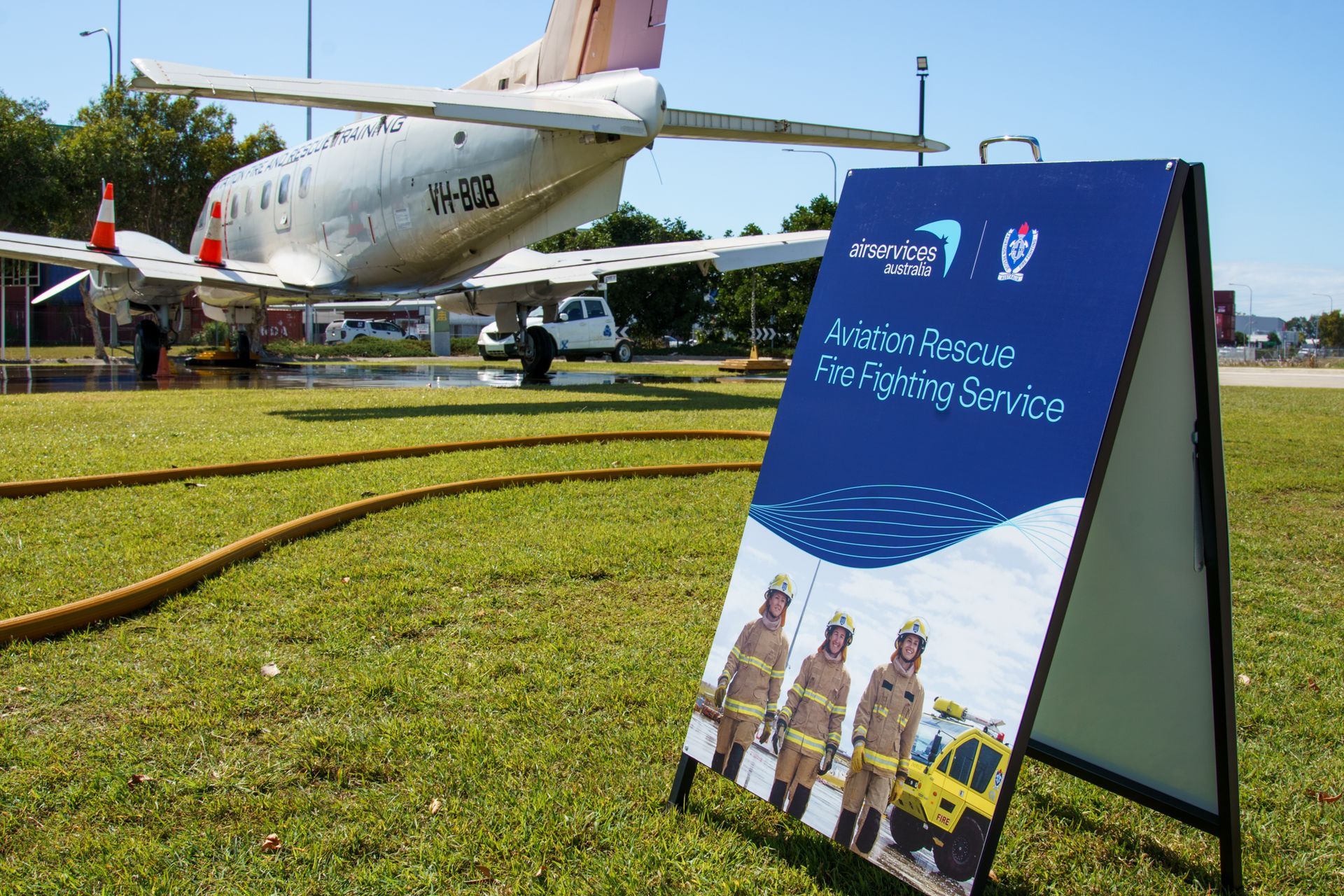 Sign for Aviation Rescue Fire Fighting Service on a grassy field with an airplane in the background.
