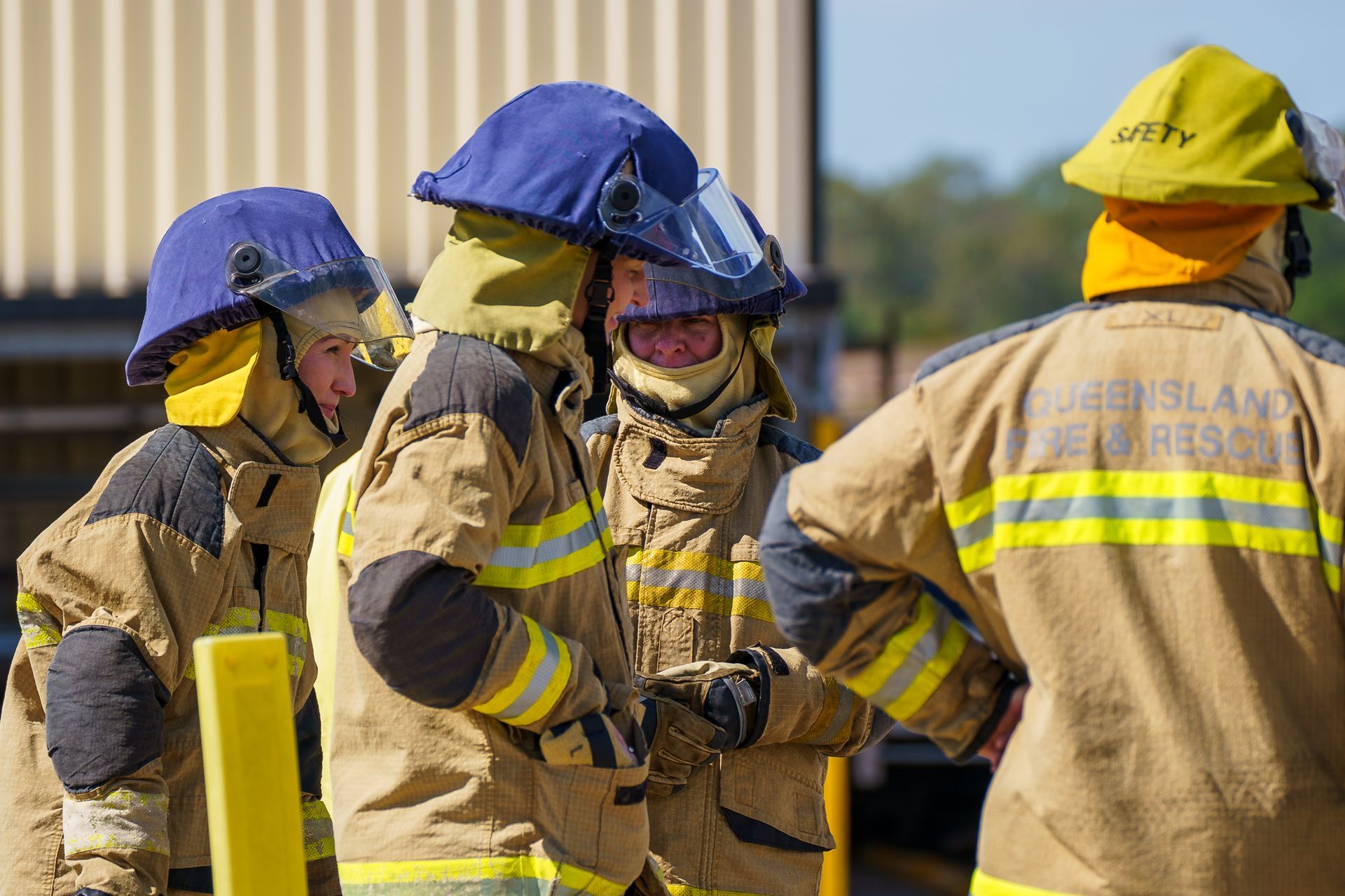 Firefighters in protective gear, preparing outdoors. Blue and yellow helmets, tan suits.