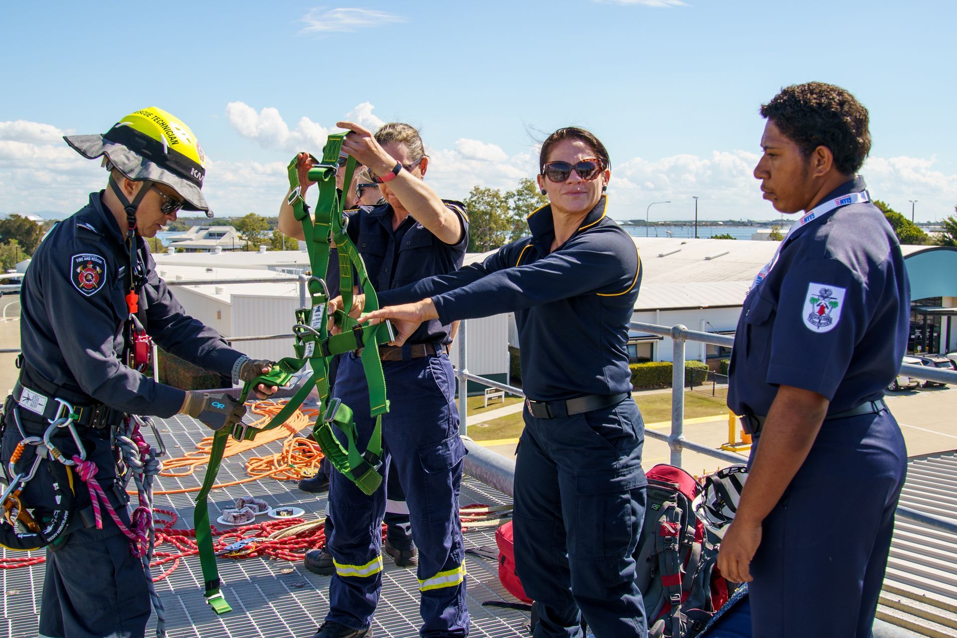 Firefighters on a rooftop practice with a safety harness under a blue sky.