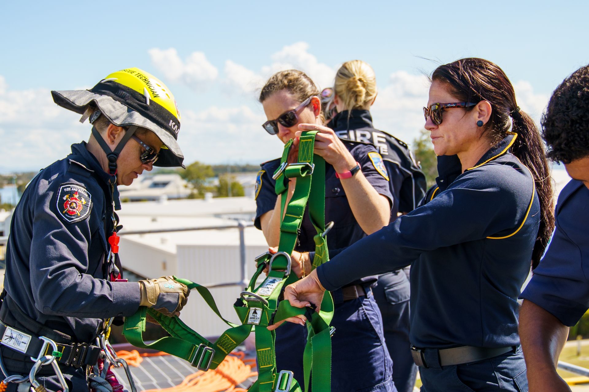 Firefighters training on a rooftop, adjusting a green safety harness.