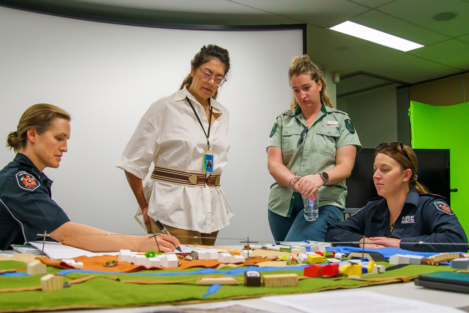 Four women in a room looking at a model, likely for planning purposes. One is holding a water bottle.