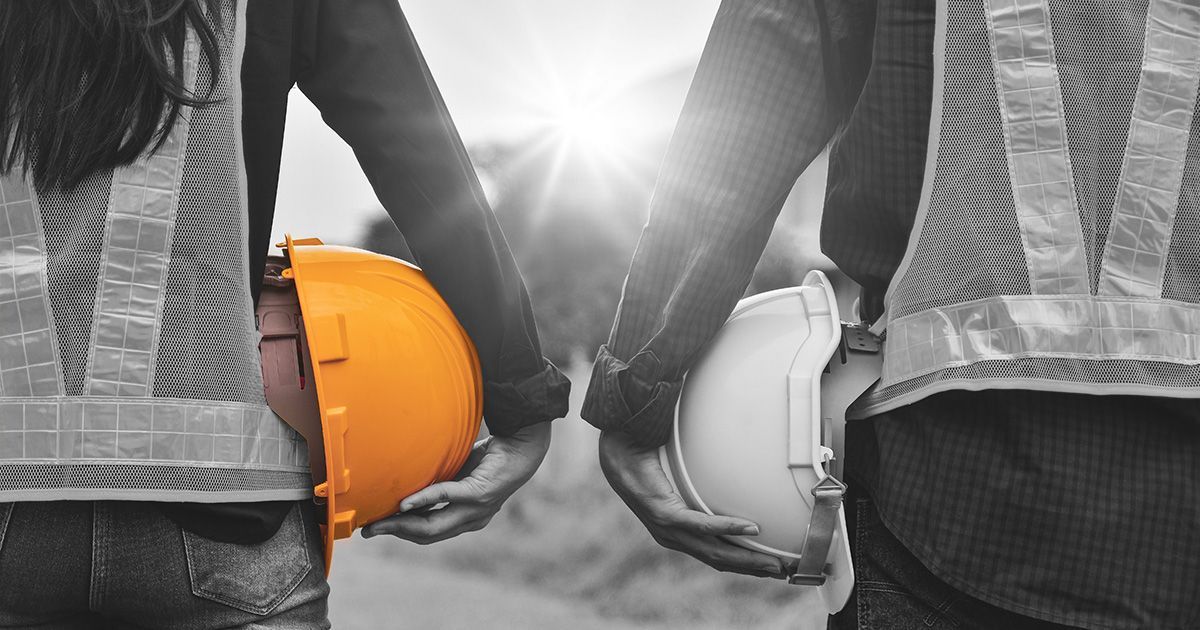 Black and white image of two contractors holding hard helmets