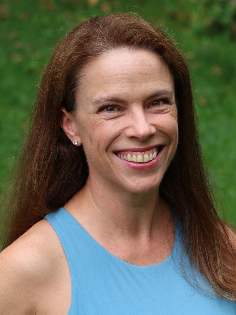 a woman with long brown hair is smiling for the camera while wearing a blue tank top .