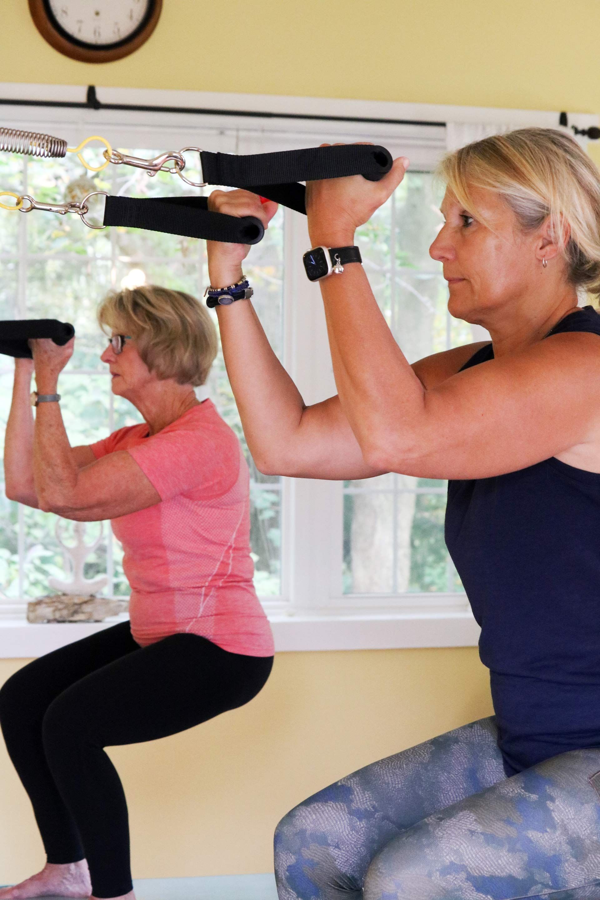 two women are doing squats on Pilates equipment