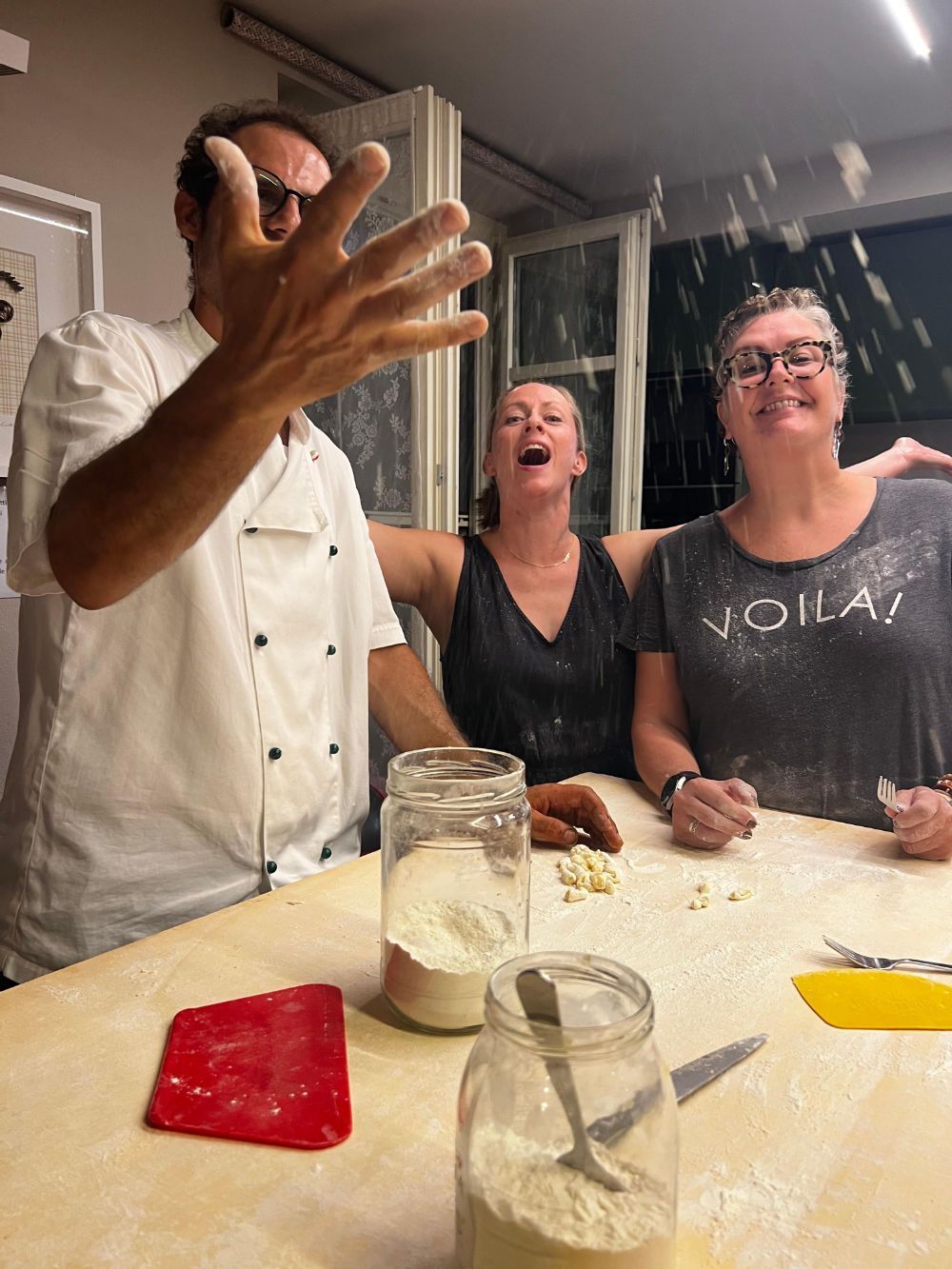 A man and two women are sitting at a table throwing flour in the air.