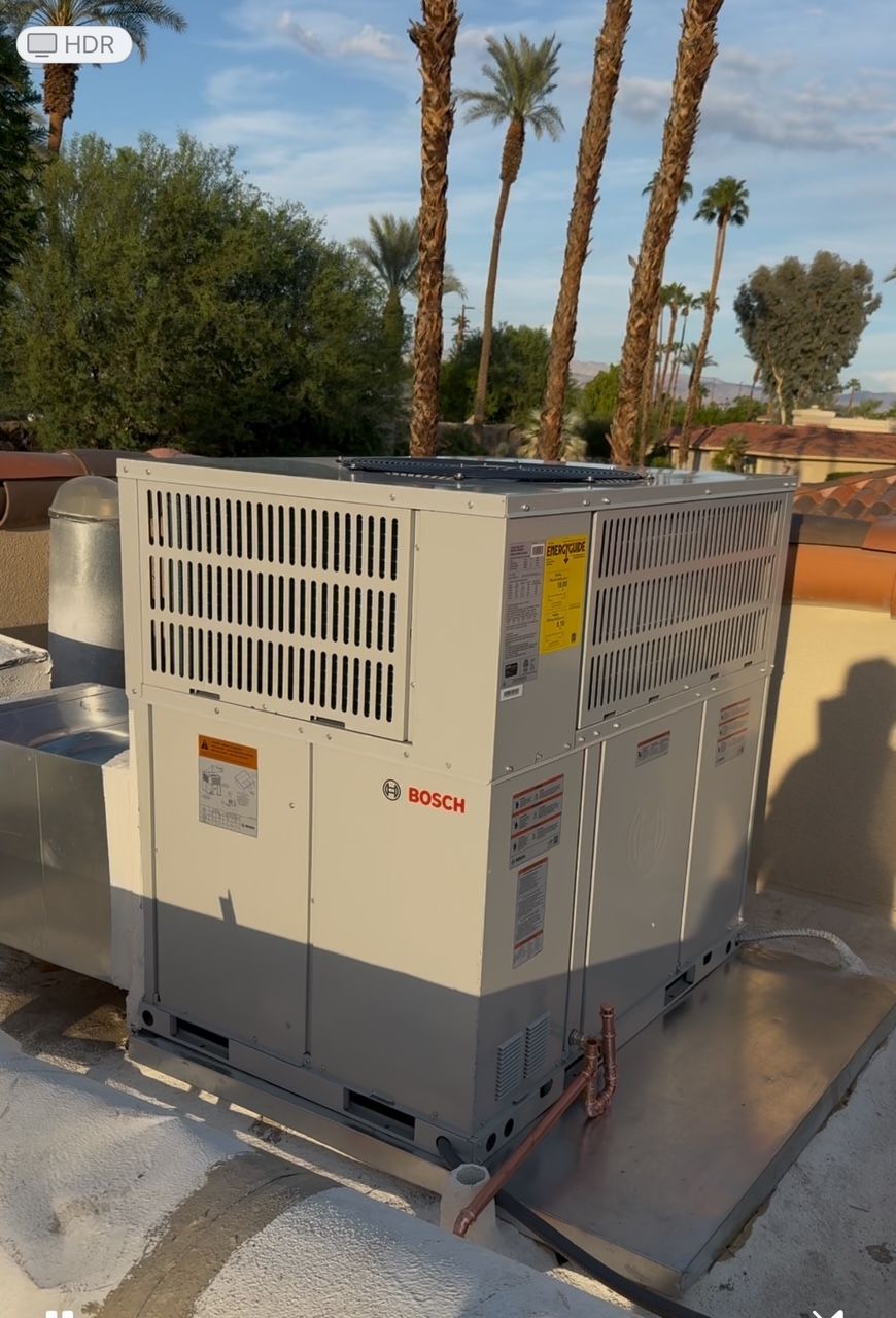 Rooftop HVAC unit on a building, with palm trees in the background under a bright sky.