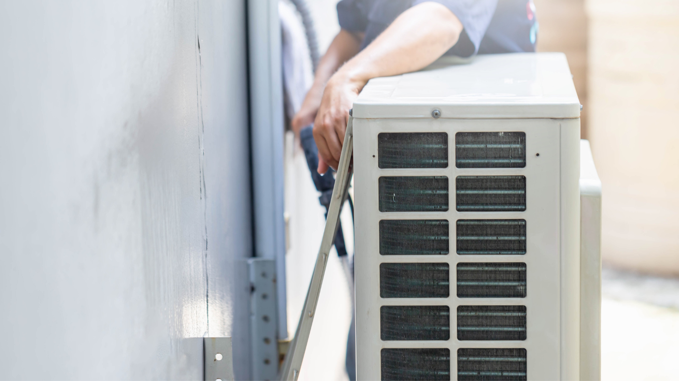 A person installs an air conditioning unit outdoors, using metal brackets.