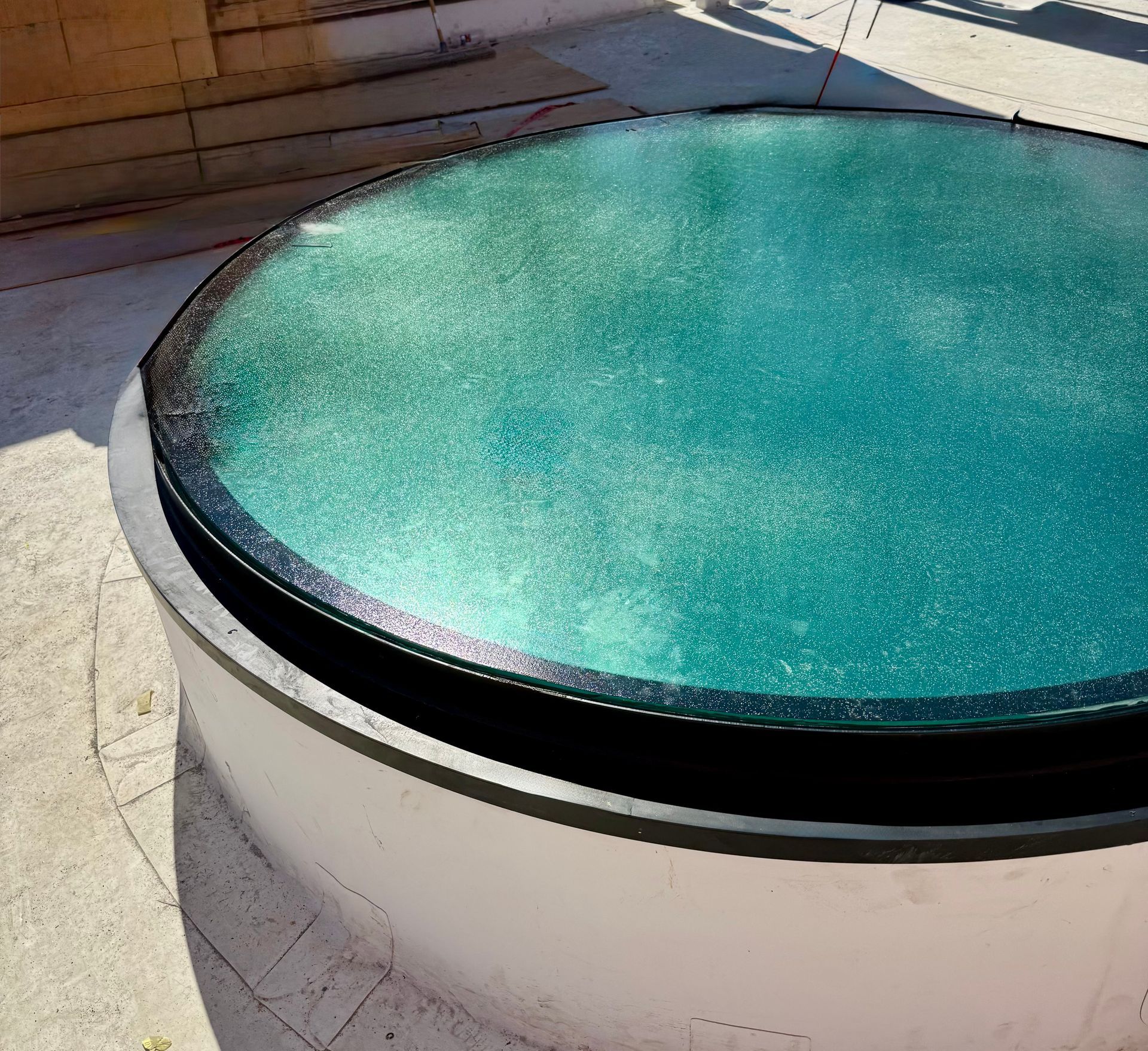 A circular, turquoise-colored pool or water feature with a dark frame, set within a concrete patio area.