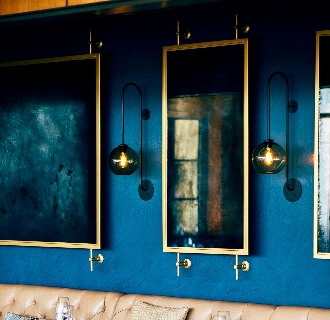 Blue wall with gold-framed antique mirrors and sconces. Beige seating below.