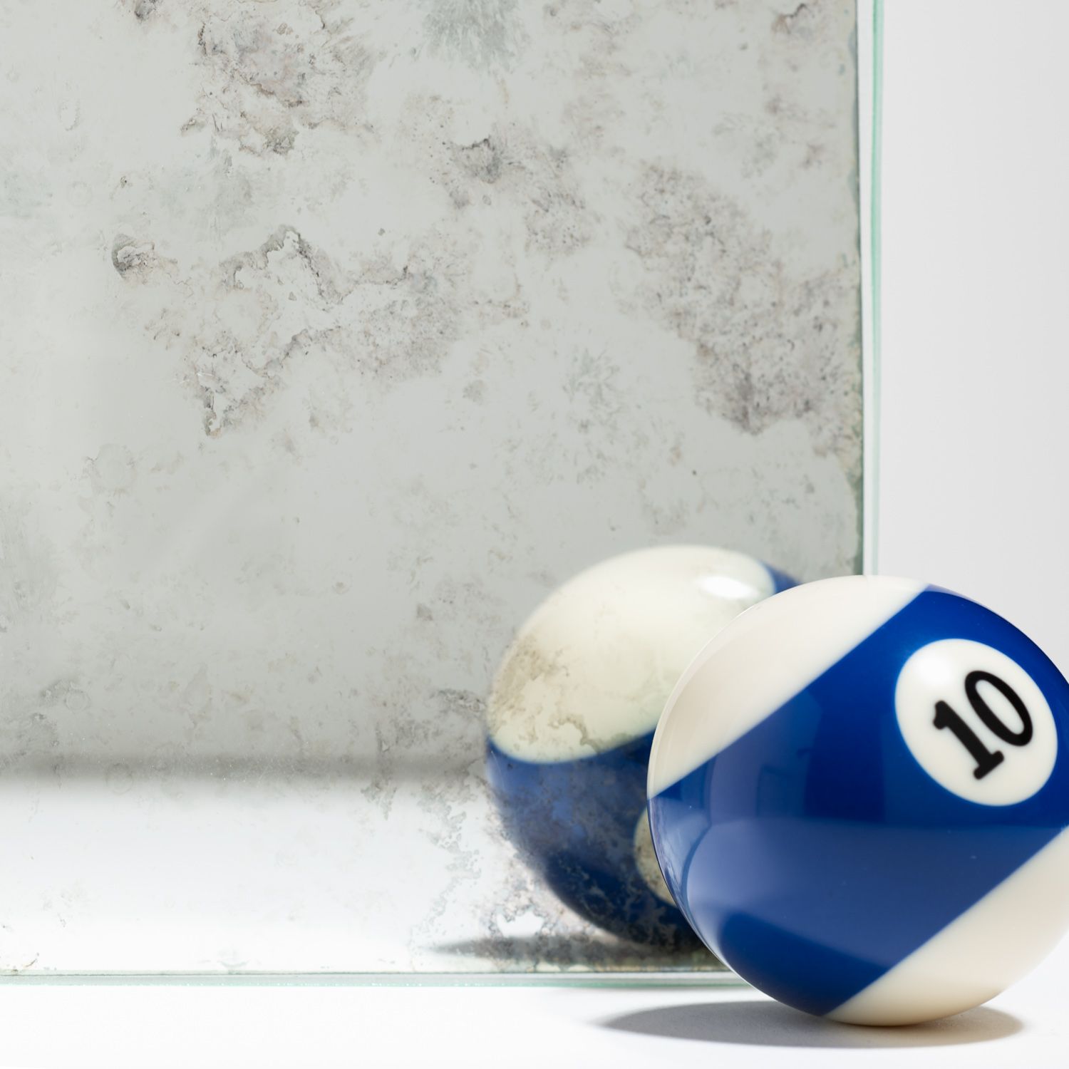 A blue and white number 10 billiard ball sits against an antique, weathered mirror, showing its reflection.