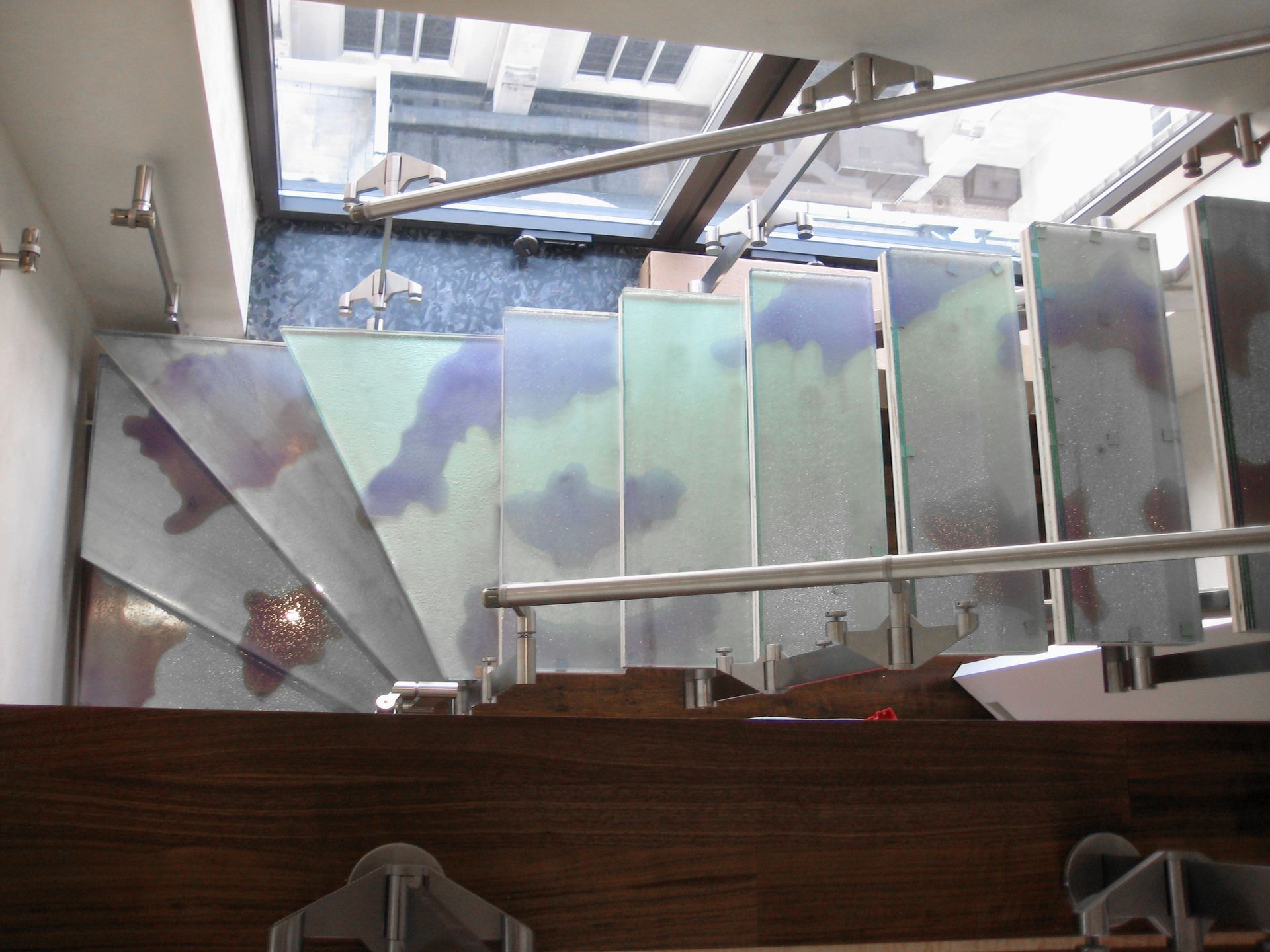 Top-down view of a modern staircase with translucent, patterned glass treads and a stainless steel handrail.