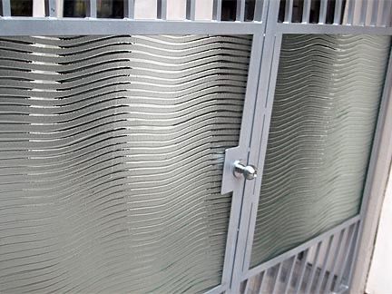 Metal gate with wavy mesh panels, secured with a latch, likely an entry point.