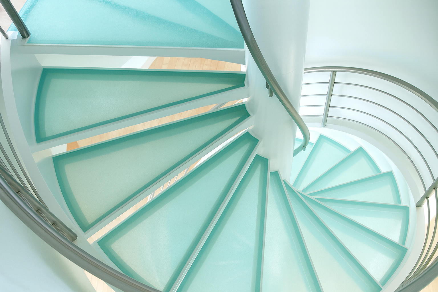 Spiral staircase with aqua-colored glass steps, silver railing, and a white central support.