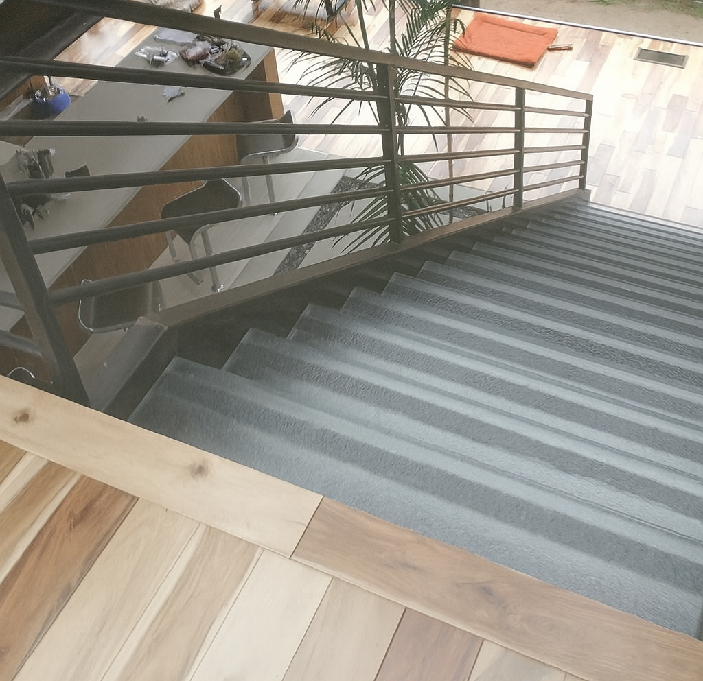 Staircase with metal railing leading up, light wood and gray stairs.