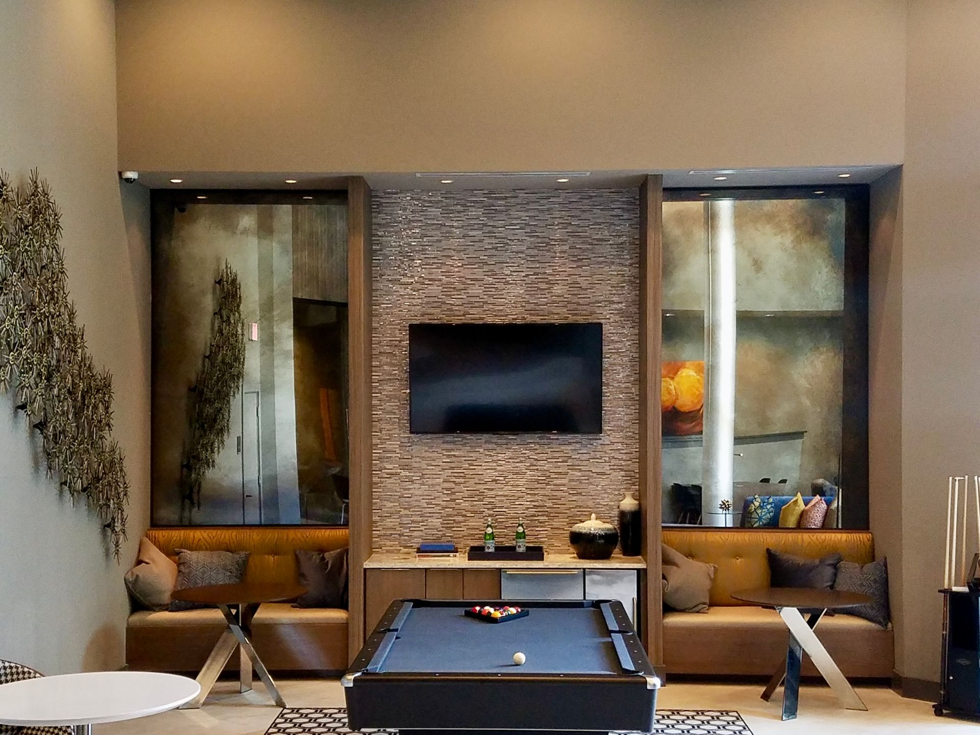 A modern lounge area with a pool table, tan built-in bench seating, and a mounted TV on a stone wall.
