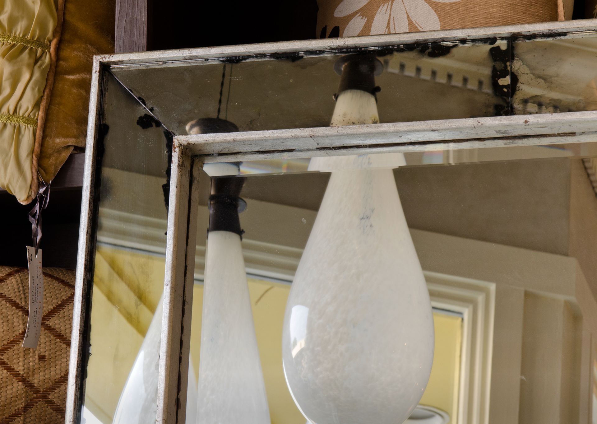 A pair of white lamps are sitting in front of a framed antique mirror