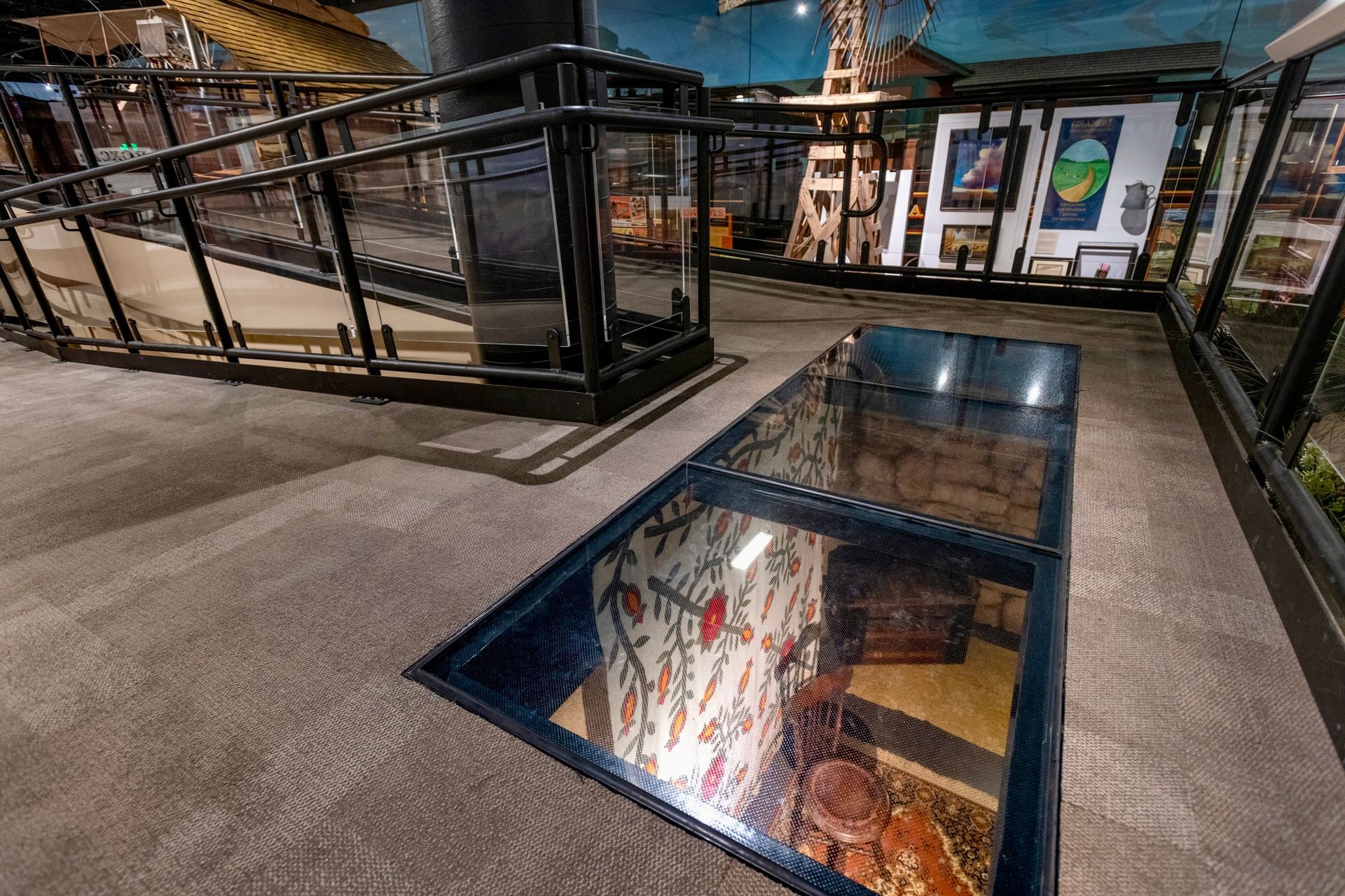 Museum exhibit with a glass floor panel revealing objects below. Ramps and railings are visible.