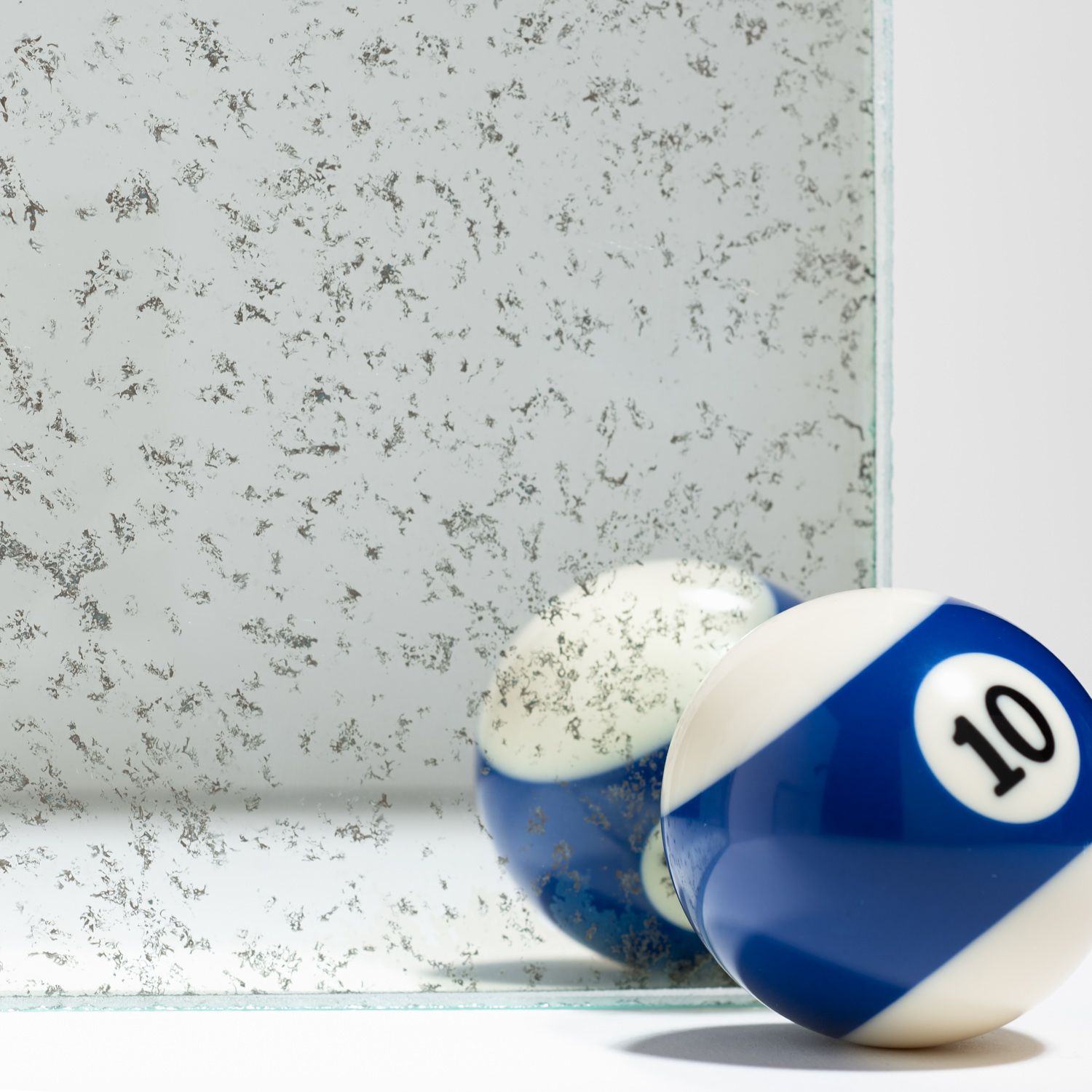A blue and white number 10 billiard ball sits next to a reflective glass surface, showing its reflection.