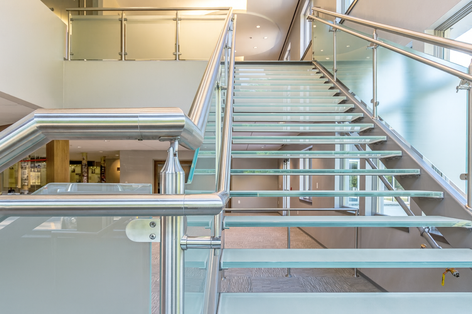 Glass staircase with metal railings and frosted glass panels in a modern building.