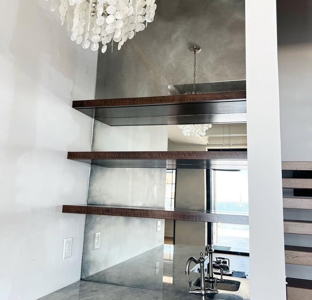 Mirrored wall with wooden shelves, a decorative chandelier, and a view through a window.